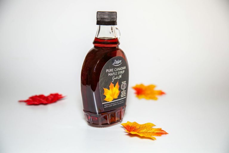 Close-up of a Canadian maple syrup bottle with colorful autumn leaves on white background.