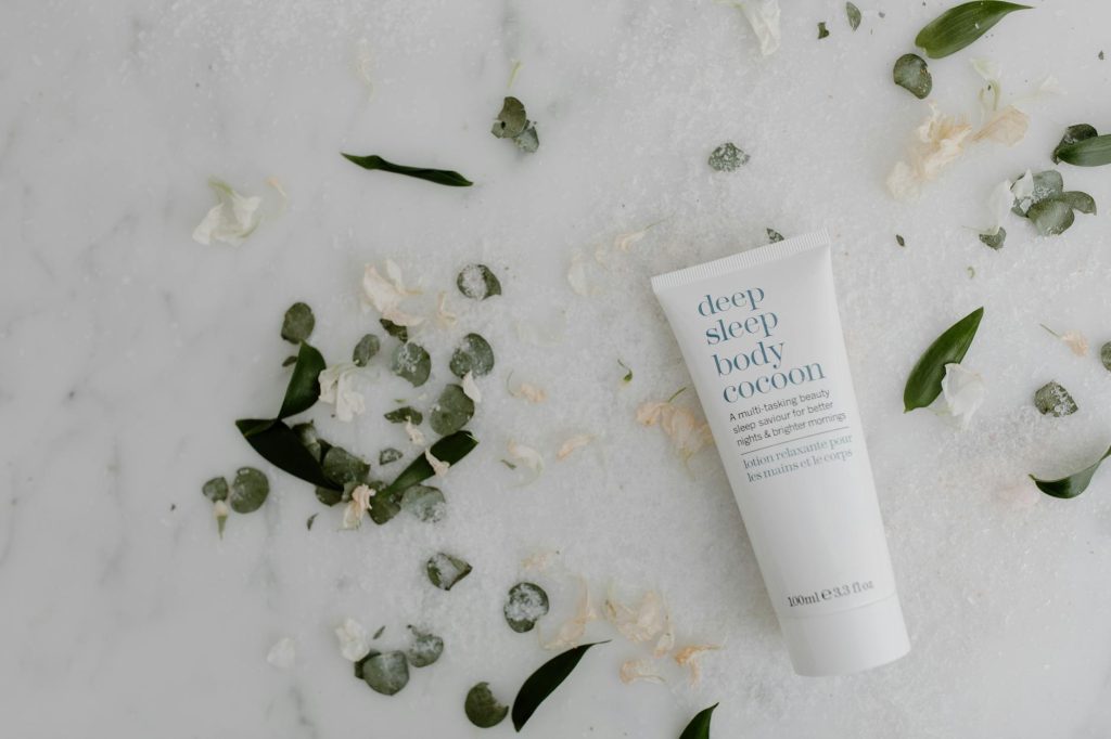 Flat lay of soothing sleep lotion surrounded by green leaves on marble, perfect for skincare themes.