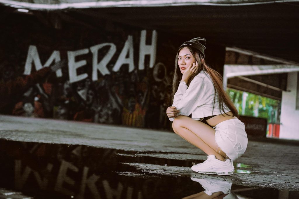 Young woman crouching in an urban setting with graffiti backdrop.