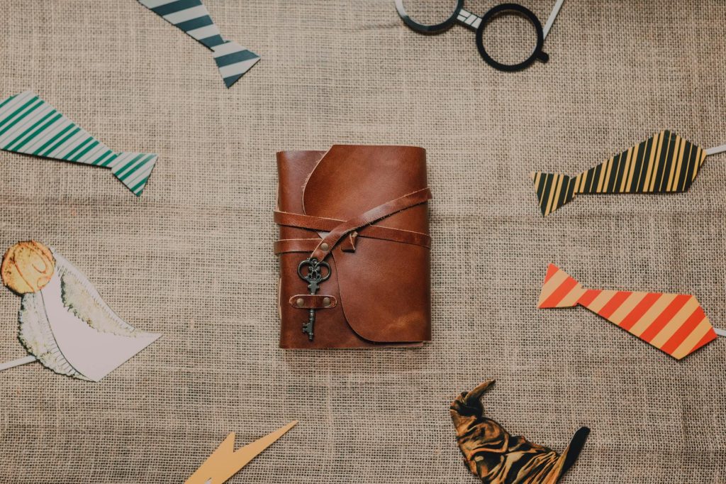 Leather journal wrapped with key, surrounded by Harry Potter themed items on rustic textile background.