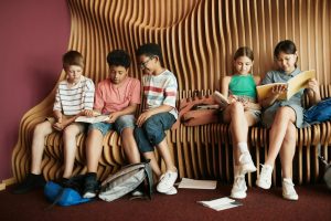 Diverse group of children reading books on a stylish wooden bench indoors.