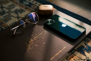 Stylish desk setup featuring notebook, sunglasses, smartphone, and headphones in soft natural lighting.