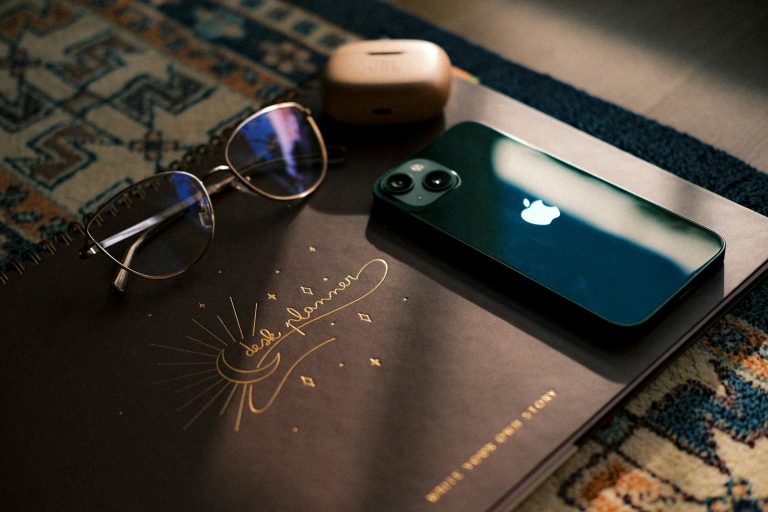 Stylish desk setup featuring notebook, sunglasses, smartphone, and headphones in soft natural lighting.