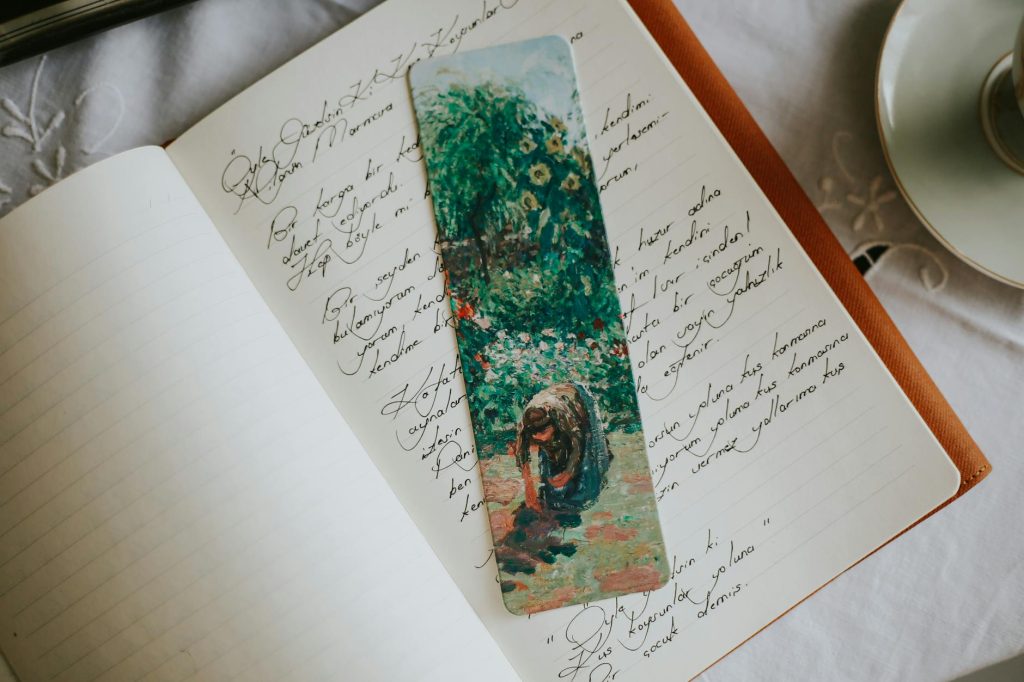 An open journal with handwriting and a colorful painted bookmark on a table.