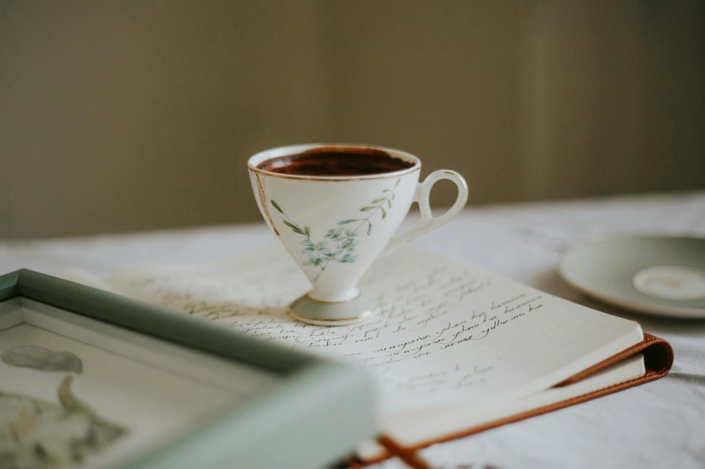 A delicate teacup with hot beverage sits on an open journal with elegant handwriting, creating a cozy scene.