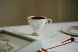 A delicate teacup with hot beverage sits on an open journal with elegant handwriting, creating a cozy scene.