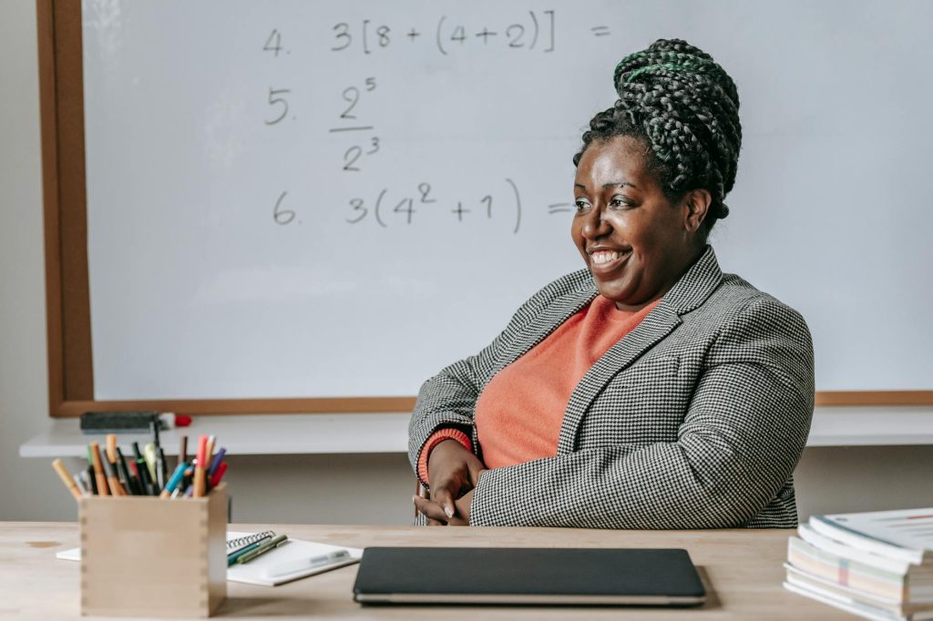 Happy African American female smiling and preparing for lesson in classroom with whiteboard