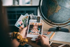 Hands holding Polaroid photos with a globe and journal, evoking travel memories.