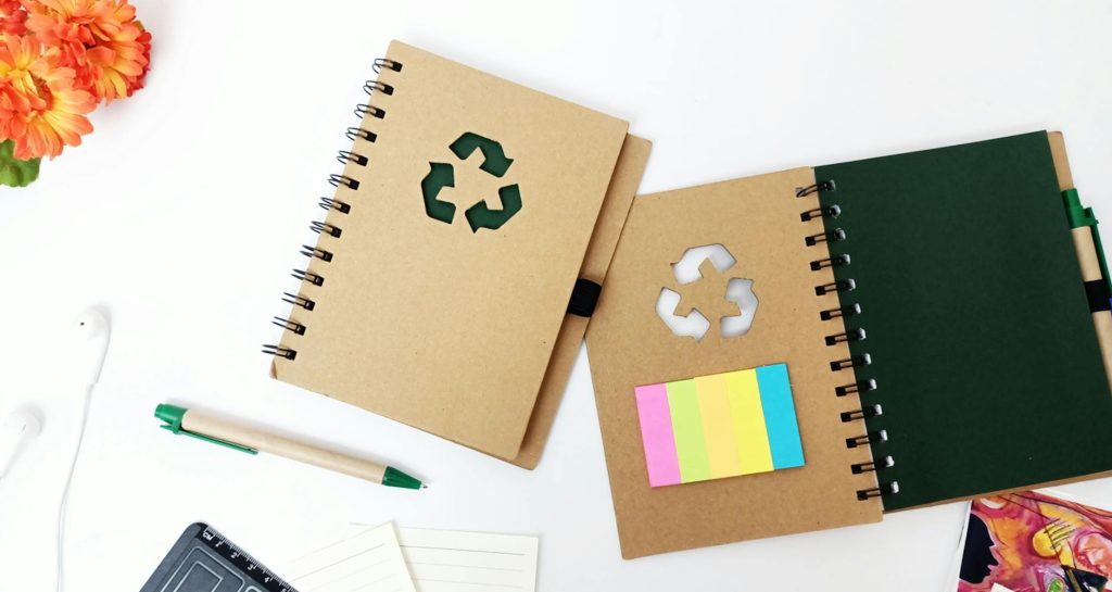 Creative flat lay of eco-friendly notebooks and stationery on a minimal white background.