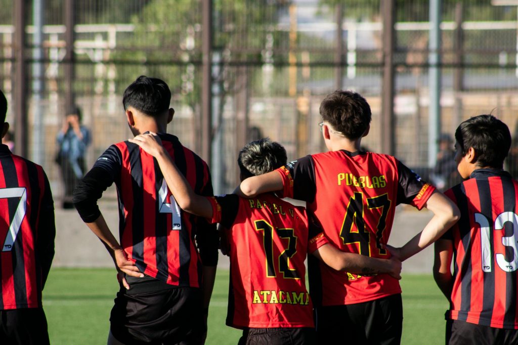 A group of teenagers huddling on a soccer field, showing teamwork and camaraderie.