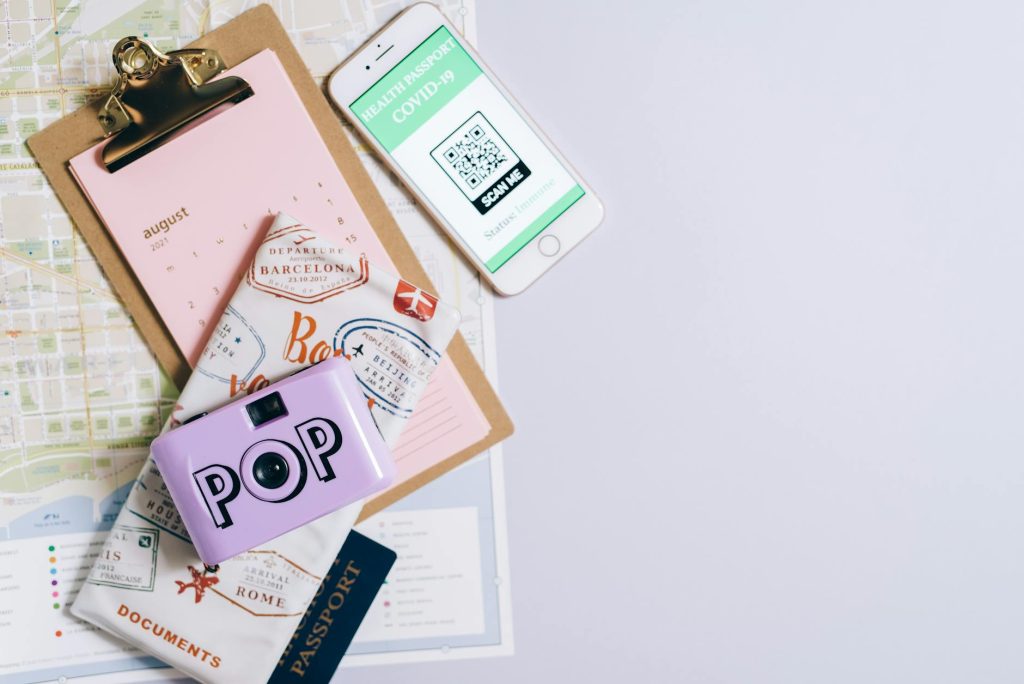 Flat lay of travel essentials including COVID-19 health passport, map, passport, and vintage camera.