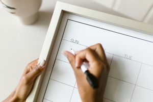 Hands holding a wall calendar, writing with a marker, organizing schedule.
