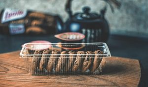 Close-up of chocolate biscotti in a plastic container with a teapot backdrop.