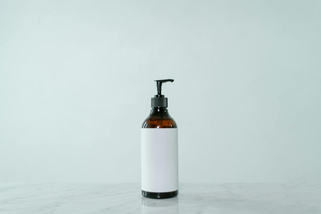 Minimalist display of a brown glass pump bottle with blank label on a light surface.