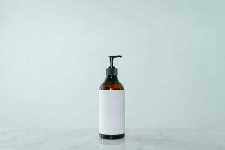 Minimalist display of a brown glass pump bottle with blank label on a light surface.
