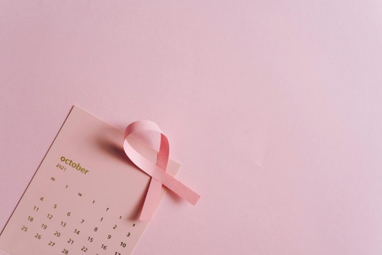 Pink ribbon on October calendar symbolizes breast cancer awareness on pastel background.