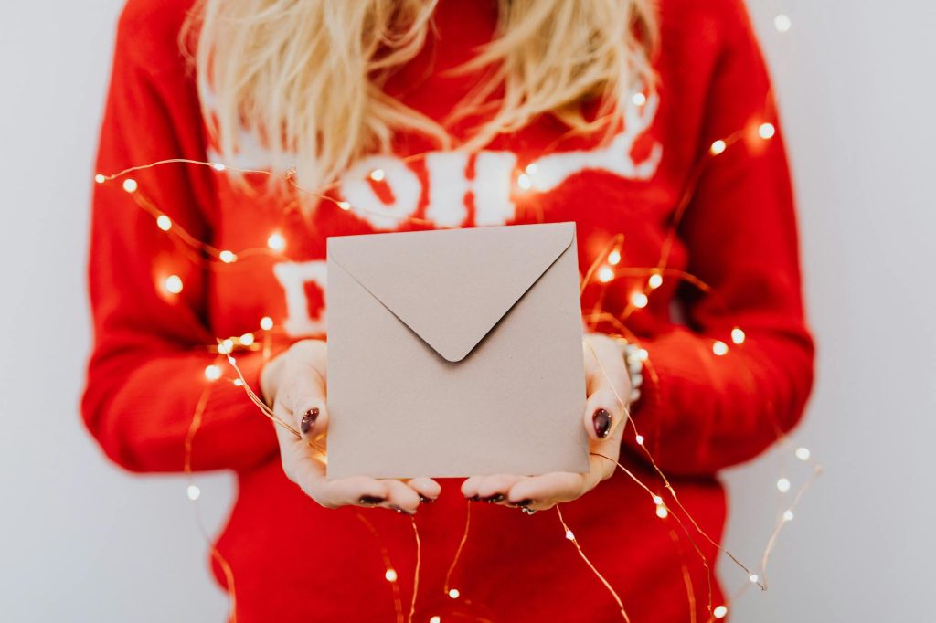Close-up of a person holding an envelope surrounded by festive lights in Christmas setting.