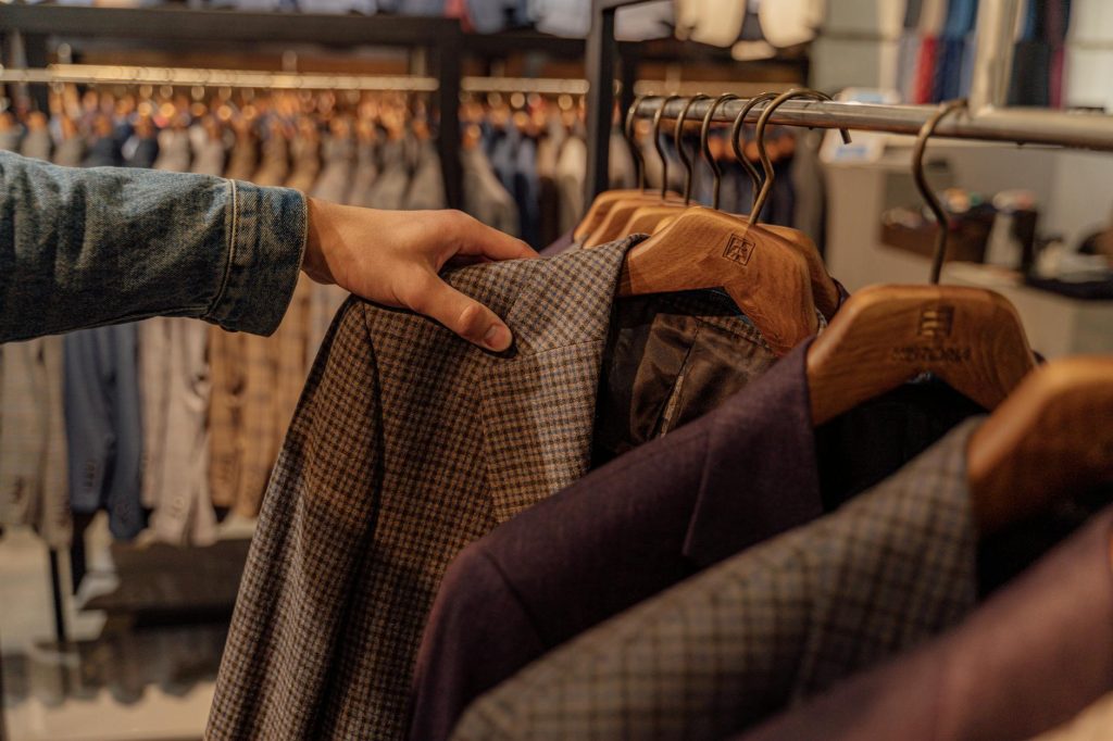 Close-up of a hand selecting men's blazers in a fashion store, highlighting trendy styles.