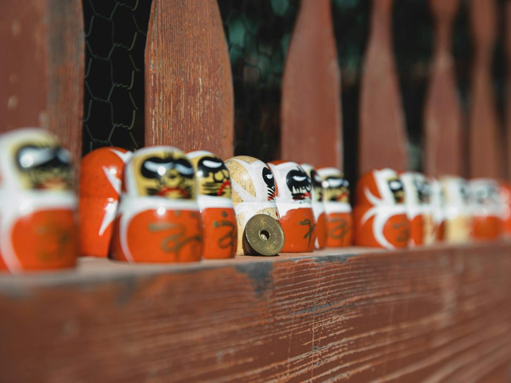 Colorful daruma dolls line up on a rustic wooden fence, symbolizing Japanese culture and tradition.