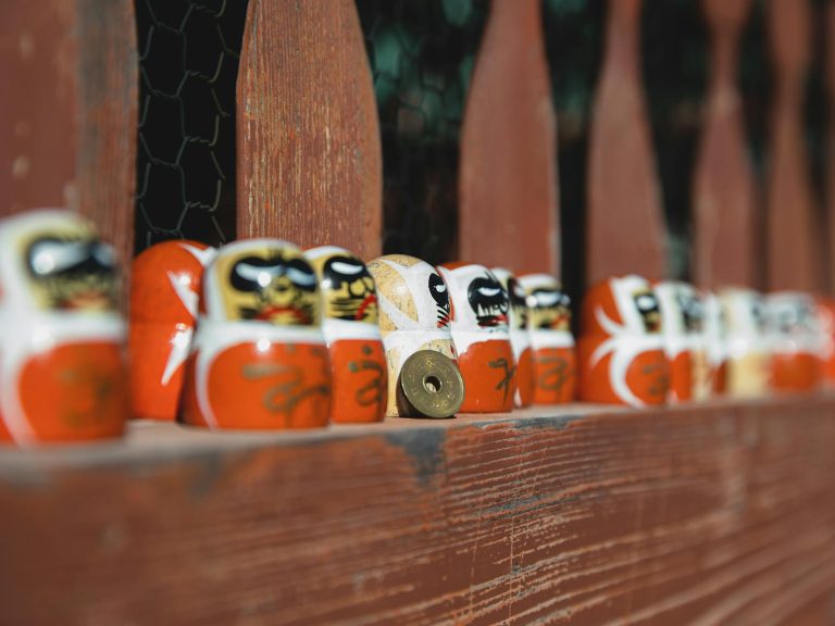 Colorful daruma dolls line up on a rustic wooden fence, symbolizing Japanese culture and tradition.