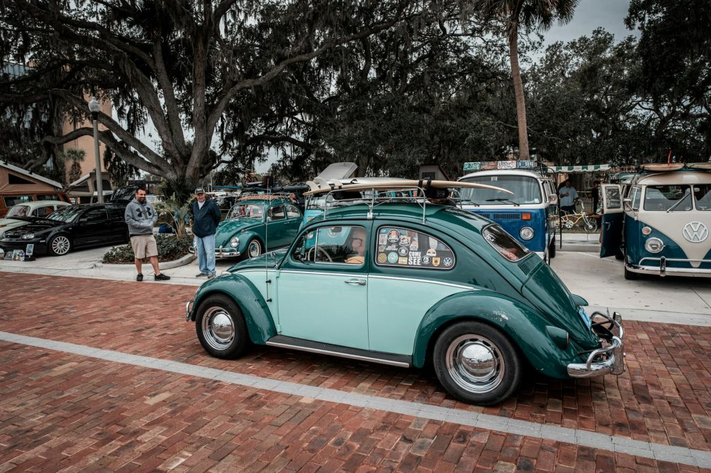 A classic green Volkswagen Beetle displayed at an outdoor vintage car show, with onlookers.