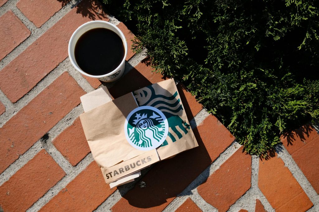 A coffee cup and Starbucks bag on a sunny brick surface in Poznań, Poland.