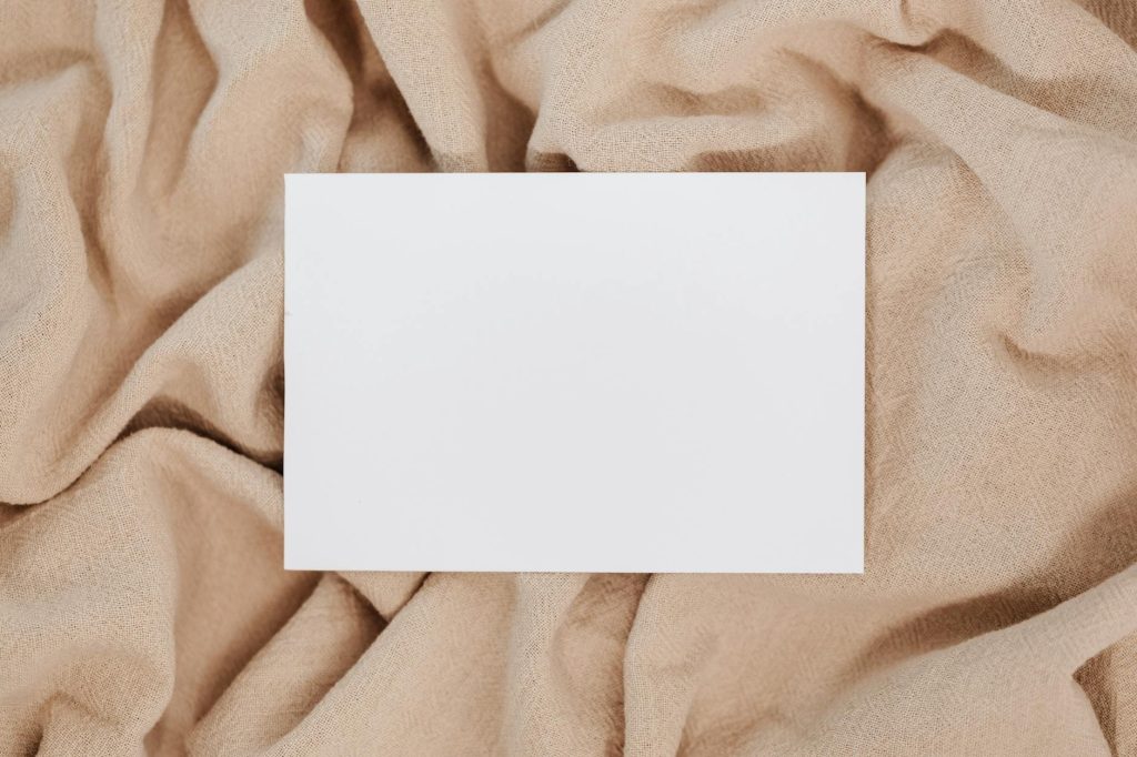 A blank white card on beige textured fabric offering space for text or design.