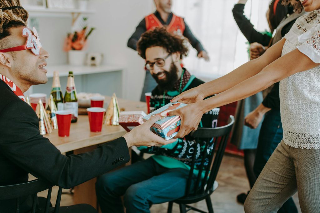 An office holiday party with adults exchanging gifts and enjoying festive decorations indoors.
