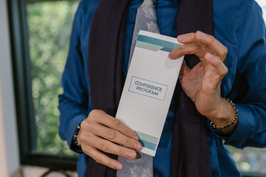 Close-up of hands holding a conference program indoors, showcasing formal attire and setting.