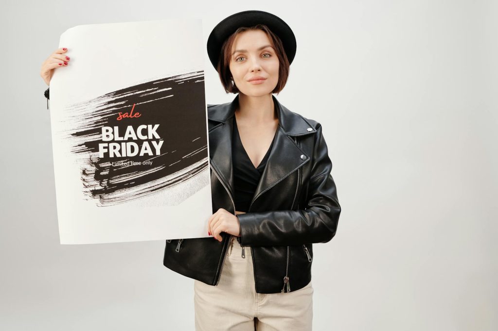 A woman in a leather jacket holding a Black Friday sale poster in a studio setting.