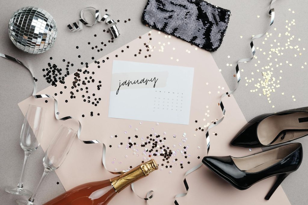 Stylish New Year flat lay featuring January calendar, champagne, high heels, and festive decor.