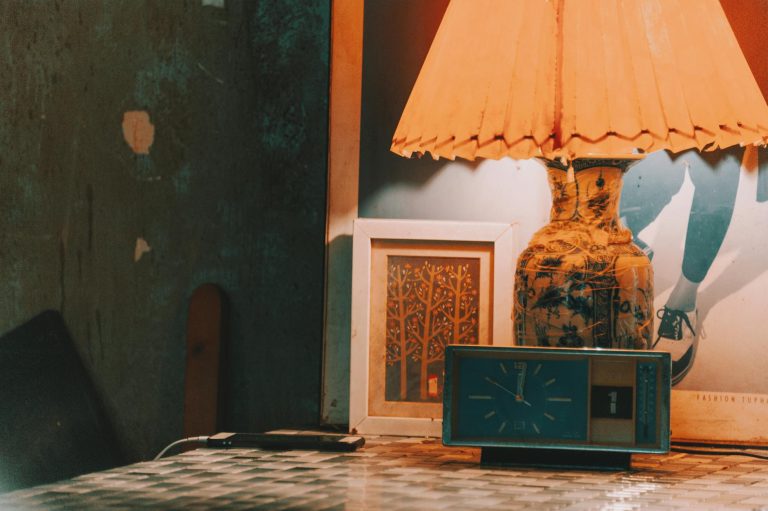 A cozy room scene with a vintage clock and a decorative lamp on a rustic surface.