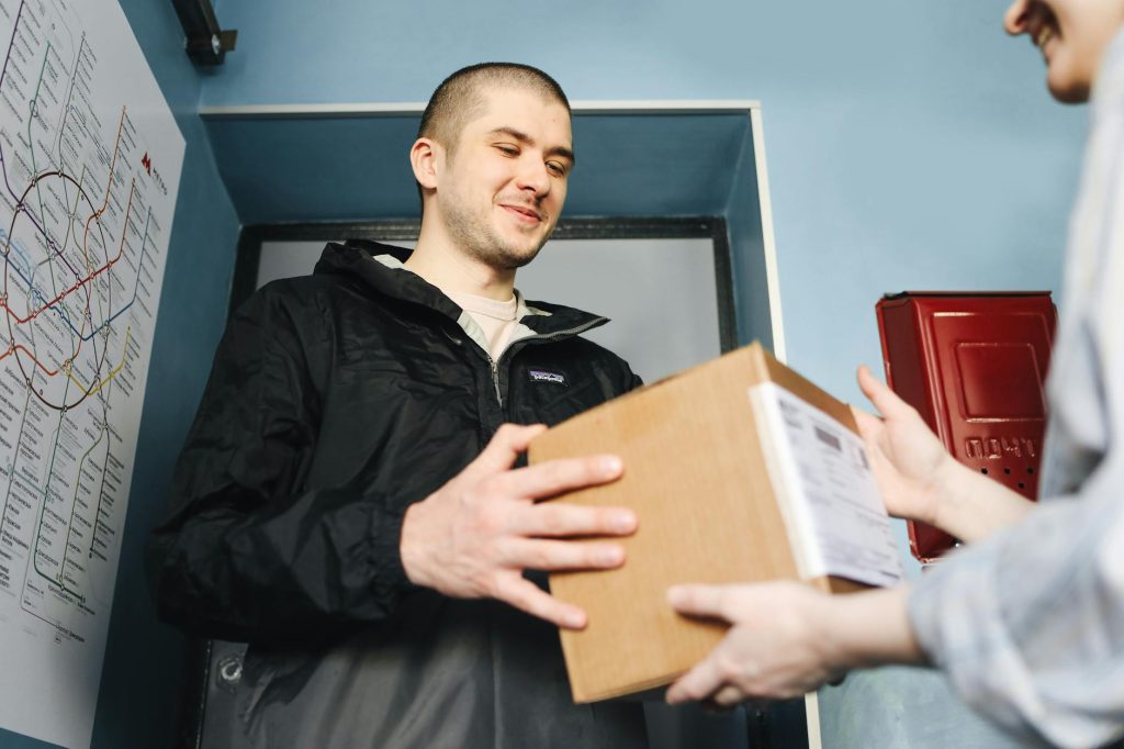 Smiling man receives a package at home apartment entrance.