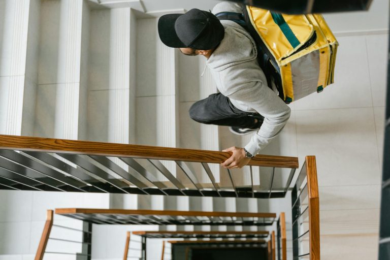 Food delivery person climbing stairs with a thermal bag, seen from above in a modern building.