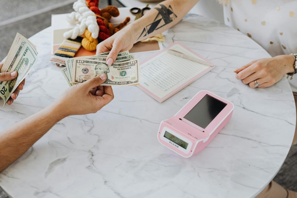 Close-up of hands exchanging US dollars over a marble table with a card reader.