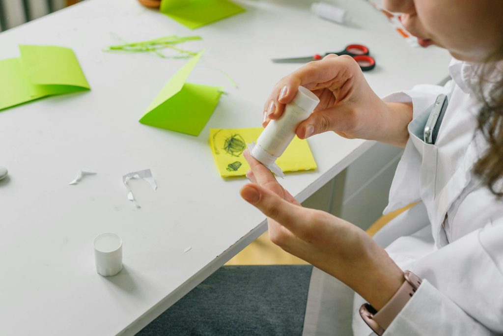 A person crafting with glue and paper at a desk, creating a handmade project.