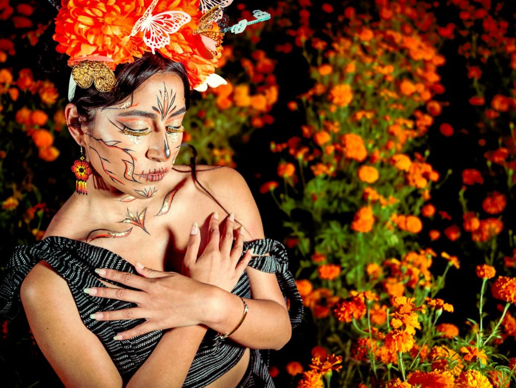 A woman with face paint in a marigold field celebrates Day of the Dead.