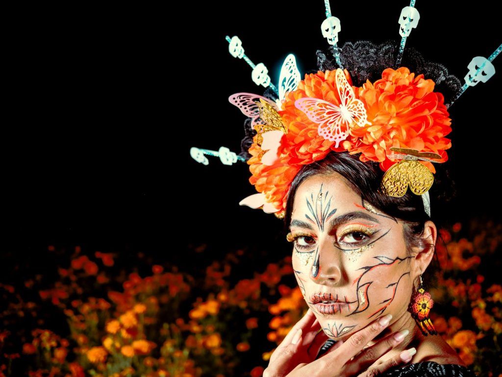 Colorful portrait featuring intricate face paint and floral headpiece for Day of the Dead.