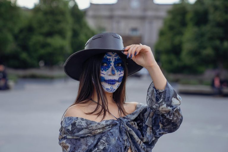 A woman wearing sugar skull makeup and a hat poses outdoors, capturing cultural artistry.