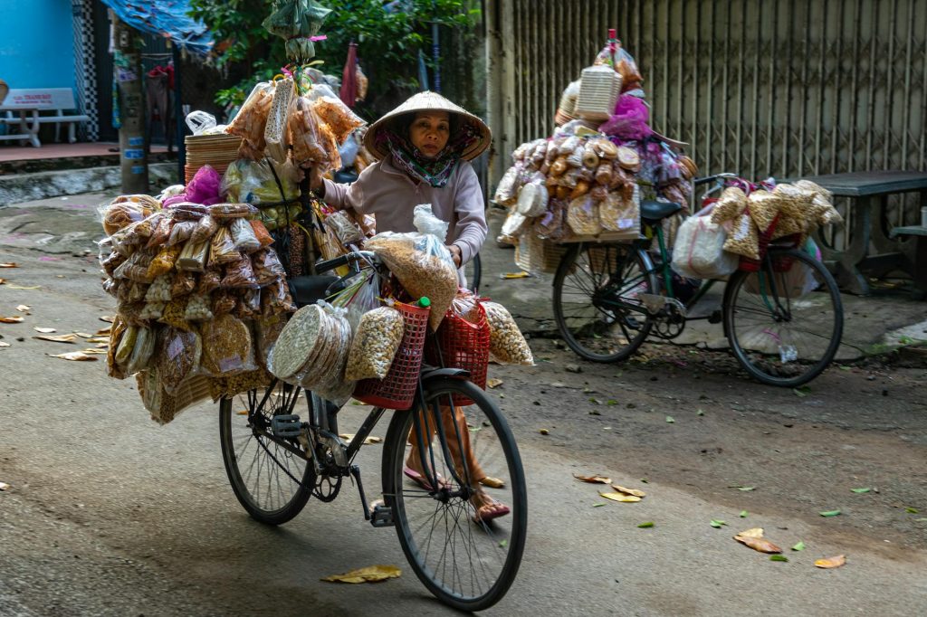 A Vietnamese street vendor rides a bicycle loaded with goods, showcasing traditional market culture.