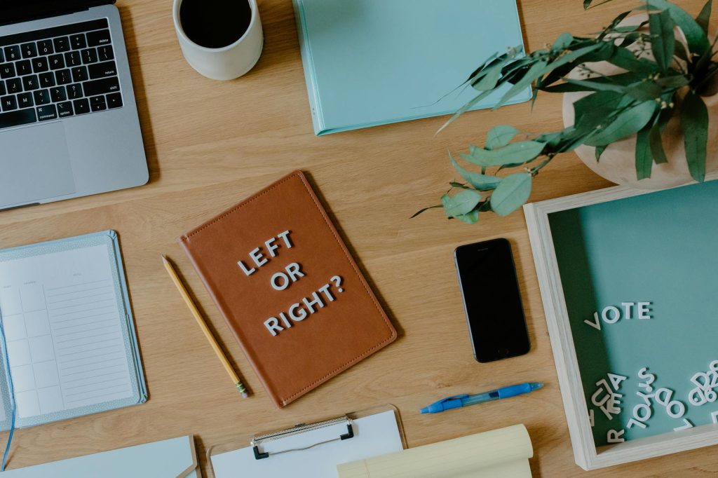Flat lay of workspace with notebook, laptop, letters spelling 'Vote', and plants in a creative setup.