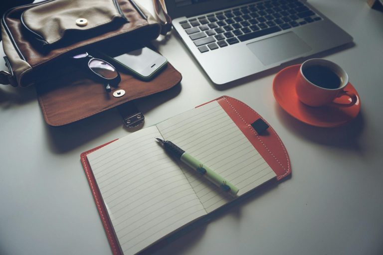 Stylish office workspace featuring a notebook, pen, laptop, and coffee cup on a tidy desk.