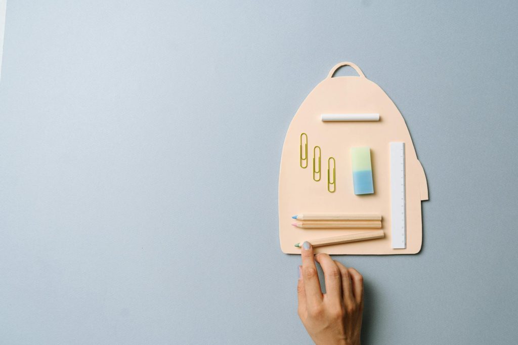 Creative flatlay of school supplies arranged on a backpack-shaped paper, showcasing creativity and organization.