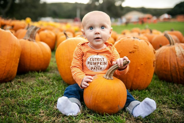 Cute infant in pumpkin patch wearing 'Cutest Pumpkin in the Patch' shirt.