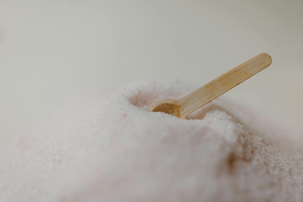 A detailed view of pink Himalayan bath salt with a wooden spoon against a soft background, ideal for spa and wellness content.