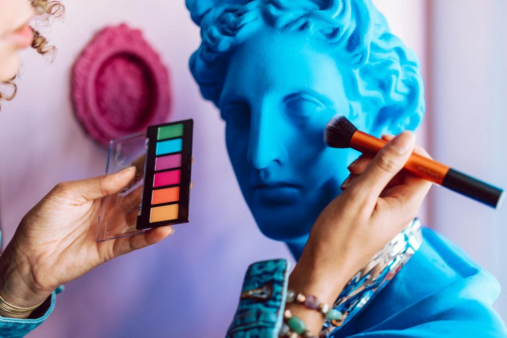 Vibrant makeup application on a blue statue bust, blending art and fashion creatively.