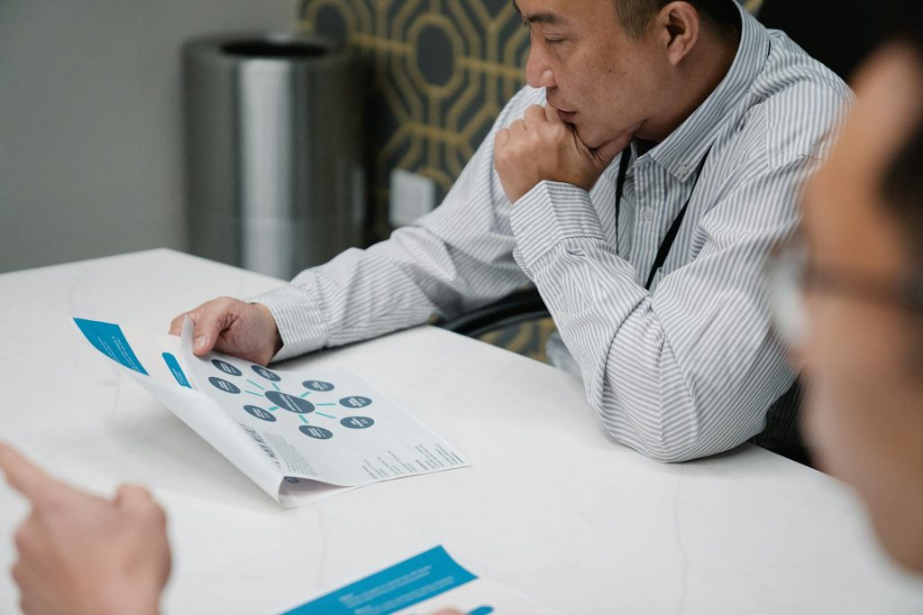 A businessman in a striped shirt thoughtfully reviews a printed document at his office desk.