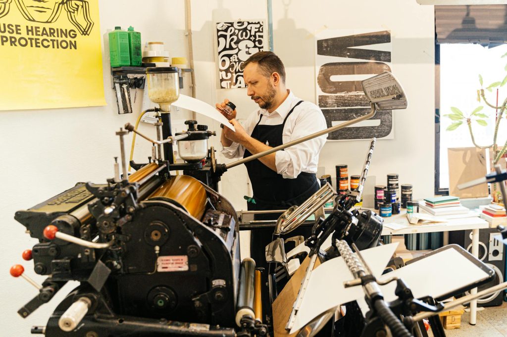 Man in apron working with vintage printing press in workshop setting, emphasizing craftsmanship.