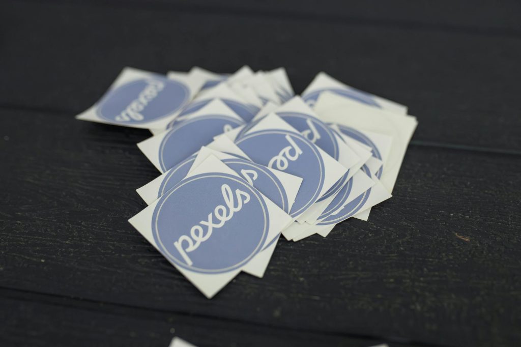 A pile of Pexels logo stickers arranged on a dark wooden surface.