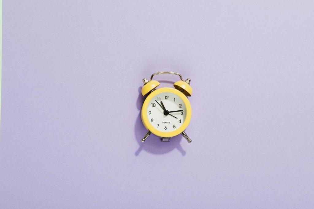 Minimalist photo of a yellow analog alarm clock on a purple background, showcasing time management concept.